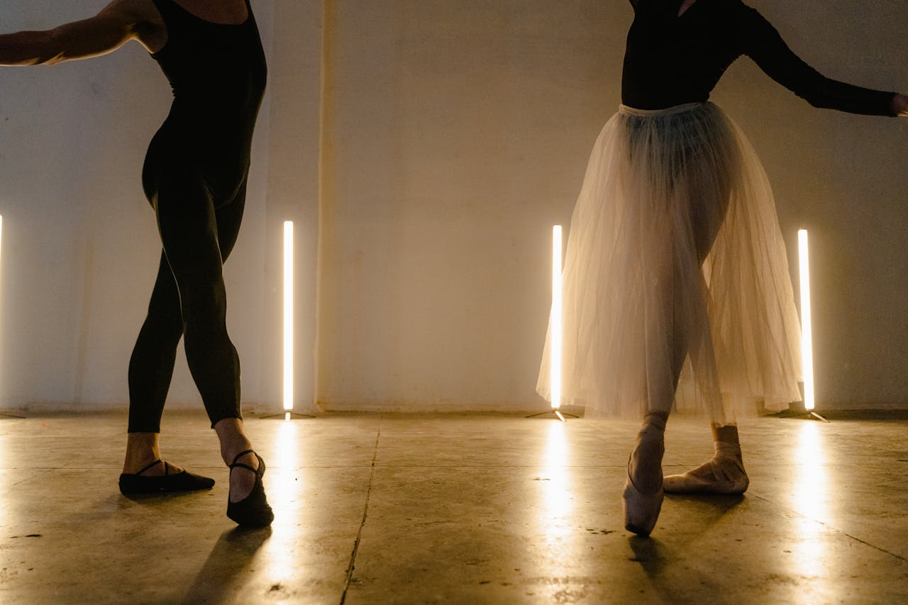Two ballet dancers practicing graceful poses in a dimly lit dance studio.